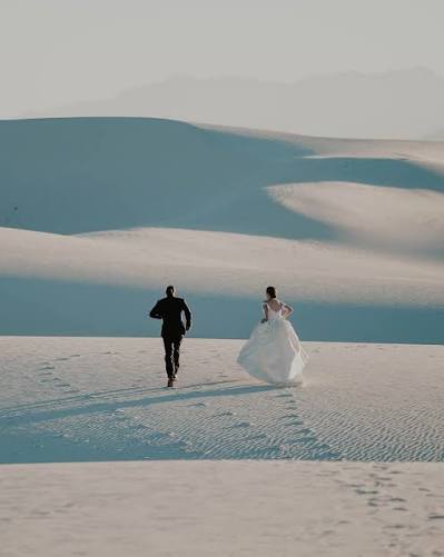 A bride and groom running across pale sand dunes